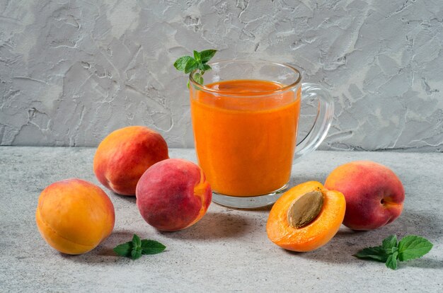 Frischer Aprikosen-Smoothie in einer Glasschale und frische Aprikosen auf einer grauen strukturierten Wand.