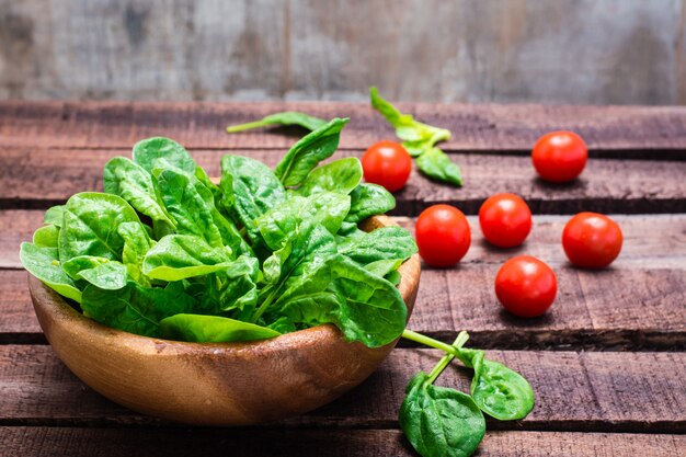 Frischer babyspinat verlässt in einer schüssel und in kirschtomaten auf einem holztisch