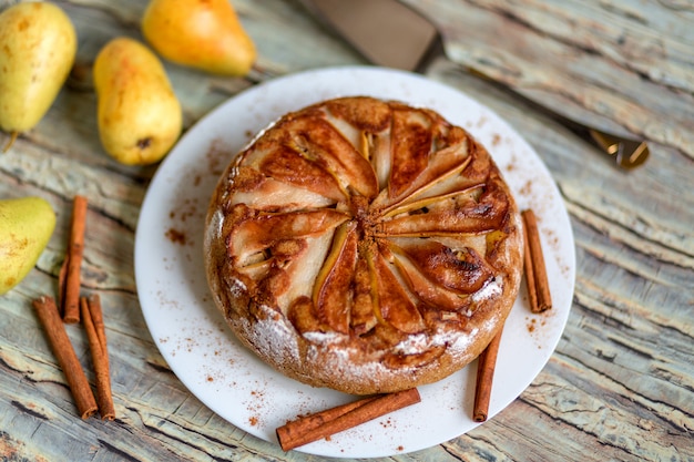 Frischer Birnenkuchen auf einer weißen Platte, verziert mit Zimt, frischen Birnen und Gewürzen auf einem hölzernen Hintergrund