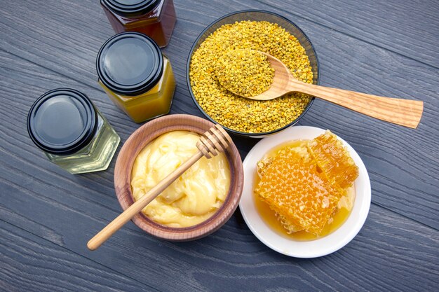 Foto frischer blumenhonig verschiedener sorten, pollen und waben mit löffeln auf holzhintergrund. bio-vitamin-gesundheitsnahrung