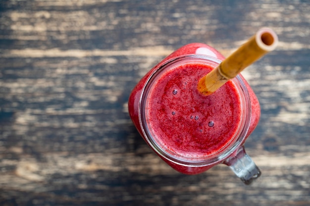 Frischer Brombeer-Smoothie im Glas mit Bambusstroh auf hölzernem Hintergrund. Draufsicht, Nahaufnahme, Kopierraum. Gesundes Lebensmittelkonzept