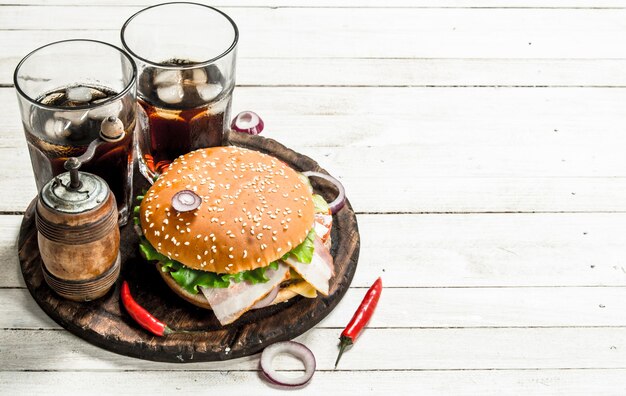 Frischer Burger mit Cola auf einem Holzbrett. Auf einem weißen Holztisch.