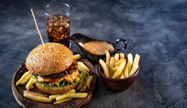 Frischer Burger mit knusprigen Pommes Frites in der Nähe von Getränke- und Saucenboot