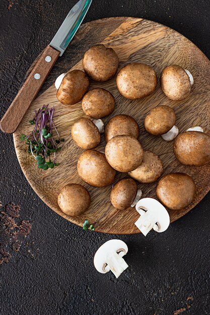 Frischer Champignon auf Holzteller, dunkelbrauner Hintergrund