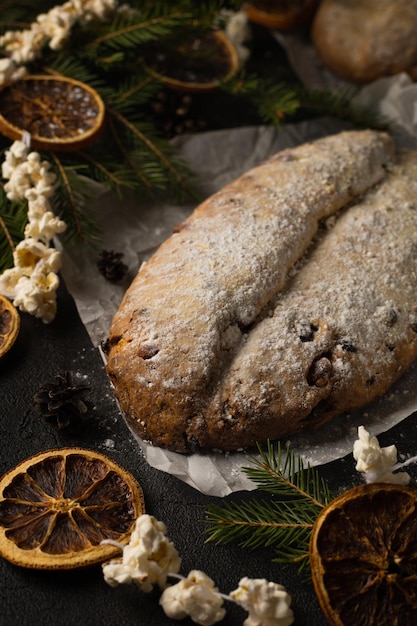 Frischer Christstollen mit getrockneten Früchten und Nüssen auf dunklem Hintergrund mit Fichte, Girlande aus getrockneten Orangen und Popcorn