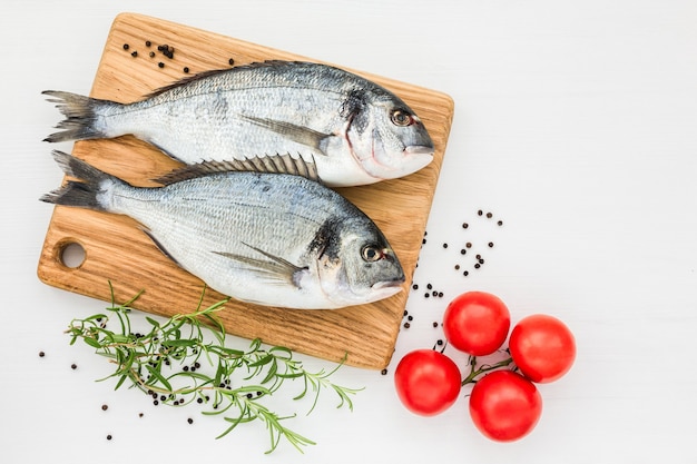 Frischer Dorado-Fisch auf hölzernem Schneidebrett mit Tomaten auf weißem Tisch. Draufsicht, Kopierraum.