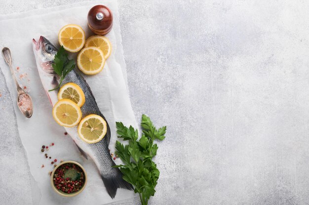 Frischer Fisch Wolfsbarsch roh mit Salzpfeffer Petersilie Olivenöl und Zitrone auf Schneidebrett auf hellgrauem Beton rustikaler Hintergrund Essen Kochen Hintergrund Draufsicht Kopierraum