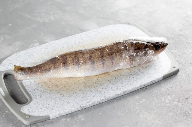 Frischer Fisch zum Einfrieren bereit. Fisch in Frischhaltefolie auf dem Tisch.