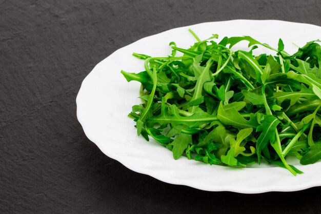 Frischer Frühlingssalat mit Rucola, in Schüssel auf dunklem Steinhintergrund mit freiem Textraum.