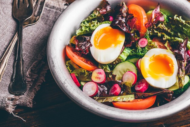 Frischer Frühlingssalat mit Tomate, Rettich, Gurke, rotem Blattsalat und gekochten Eiern in Metallschüssel