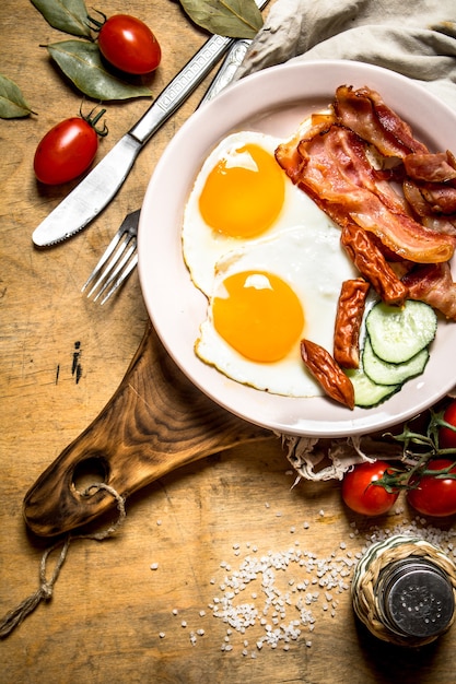 frischer Frühstücksteller. Spiegeleier mit Speck und Tomaten. Auf einem Holztisch.