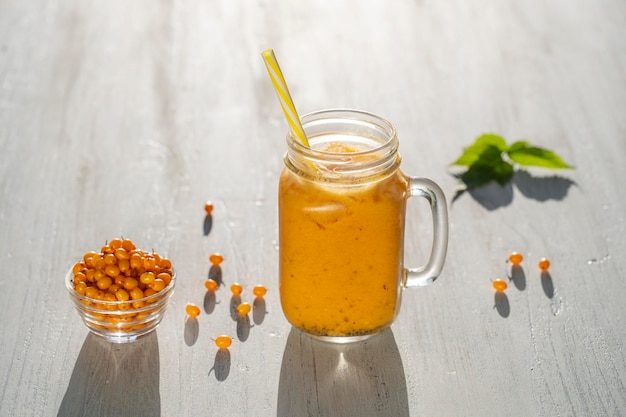 Frischer gelber Bio-Smoothie in Glasbecher auf weißem Holztisch Nahaufnahme Erfrischendes Sommerfruchtgetränk Das Konzept der gesunden Ernährung Sanddorn mit Honig und Wasser-Smoothie an sonnigen Tagen