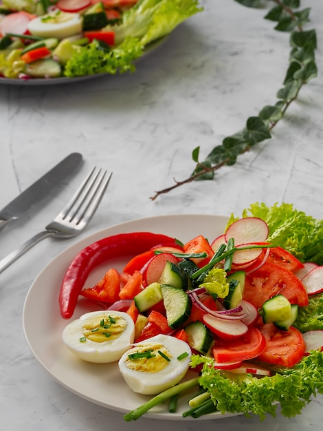 Frischer Gemüsesalat mit gekochten Eiern. Nahansicht. . Besteck auf dem Tisch.