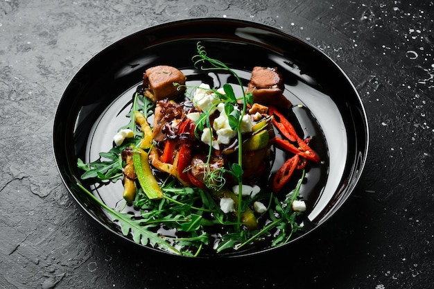 Frischer Gemüsesalat mit Kalbzucchini, Kalbfeta-Käse und Rucola auf einem schwarzen Teller im rustikalen Stil