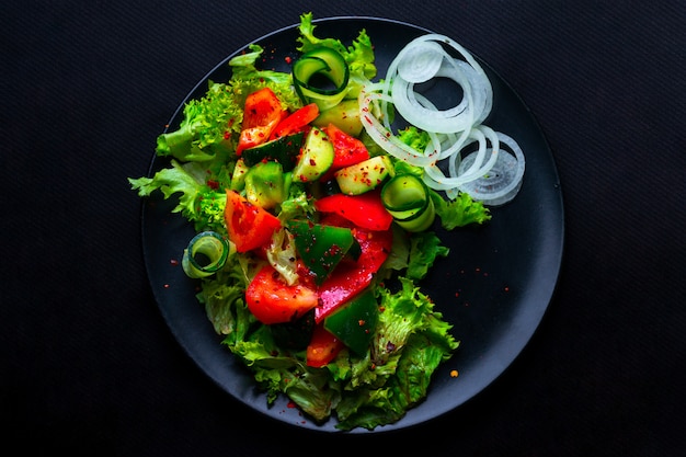 Frischer Gemüsesalat mit Purpurkohl, Weißkohl, Salat, Karotte in dunkler Tonschale auf schwarzem Hintergrund. Draufsicht