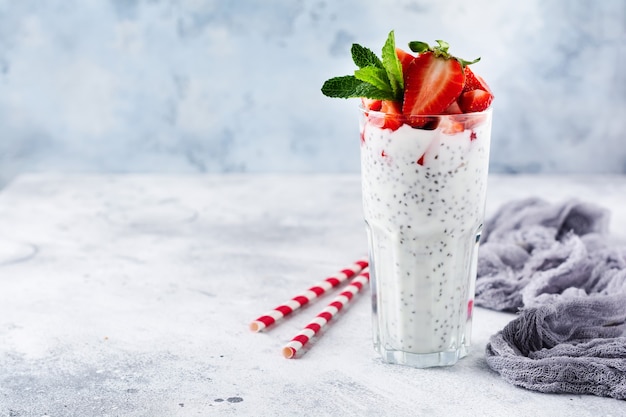 Frischer gesunder Milchshake-Joghurt mit Chiasamen und Erdbeeren in einem Becherglas gegen eine graue Betonoberfläche