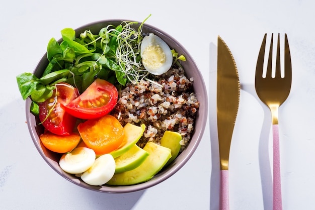 Frischer gesunder Salat mit Quinoa, Kirschtomaten und Mischgrüns, Avocado, Ei und Mikrogrüns auf Marmor