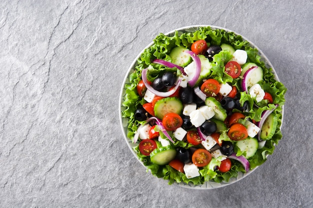 Frischer griechischer Salat in der Platte mit schwarzer Olive, Tomate, Feta, Gurke und Zwiebel auf grauem Draufsicht-Kopienraum des Hintergrundes