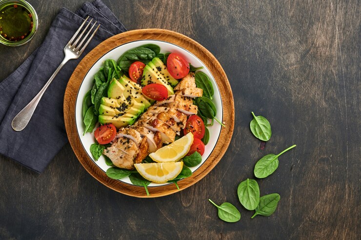 Foto frischer grüner salat mit gegrilltem hühnerfilet, spinat, tomaten, avocado, zitrone und schwarzem sesam in weißer schüssel auf altem dunklen holztischhintergrund. ernährung-diät-konzept. ansicht von oben.