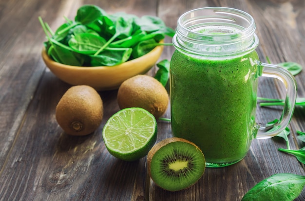 Frischer grüner Smoothie mit Kiwi, Limette und Spinat auf rustikalem Holztisch