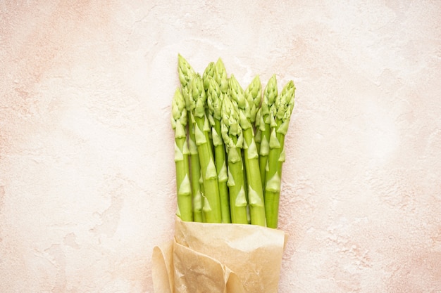 Frischer grüner Spargel in Papier auf beige Oberfläche, Nahaufnahme. Ansicht von oben