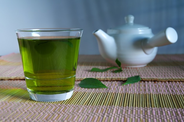 Frischer grüner Tee mit Teeblättern und Teekanne.