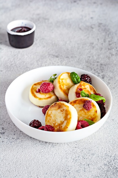 Frischer Hüttenkäse oder Ricotta-Pfannkuchen Syrnikifritters auf einem weißen Teller mit frischen Beeren und Marmelade Leckeres gesundes Hüttenkäse-Frühstück Ukrainische russische Küche süße Speisen