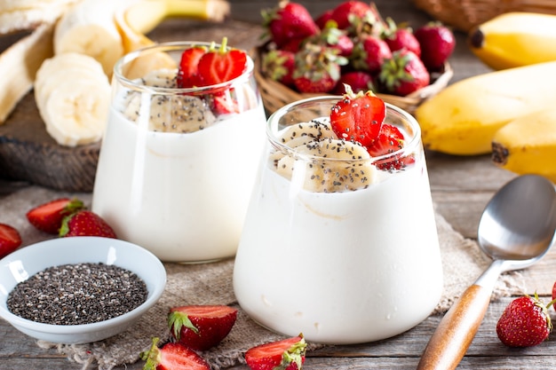 Frischer Joghurt mit Erdbeeren, Banane, Chiasamen auf einem Holztisch, leckeres Dessert zum gesunden Frühstück