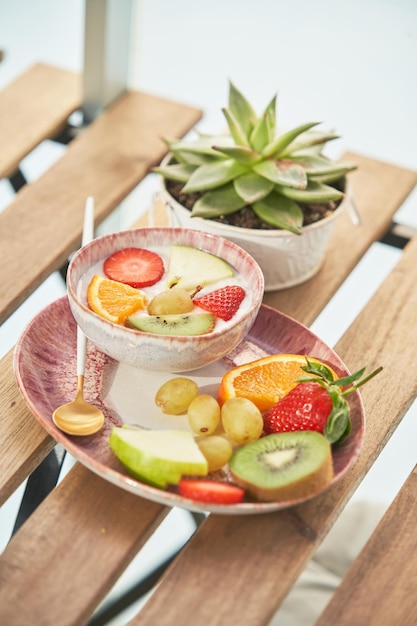 Frischer Joghurt mit Scheiben reifer Früchte und Beeren wird beim Frühstück in der Küche auf einem Holztisch mit Topfpflanzen serviert