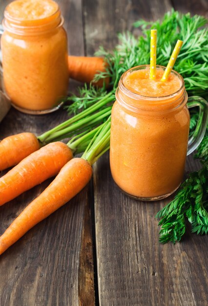 Frischer Karotten-Smoothie in Gläsern auf rustikaler Holzoberfläche.