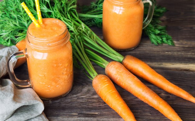 Frischer Karotten-Smoothie in Gläsern auf rustikaler Holzoberfläche.