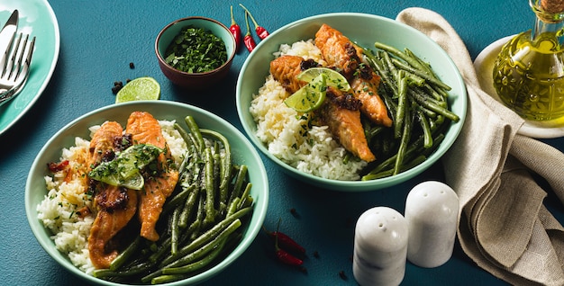 Frischer Lachs gebraten mit Ingwer und Knoblauch in Kokosmilch, mit Basmatireis und grünen Bohnen in Tellern auf dem Tisch. gesundes Rezept für die ganze Familie.