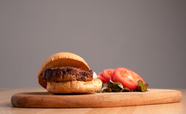 Foto frischer, lecker hausgemachter hamburger mit frischem käse neben geschnittenen tomaten auf einem schneidbrett