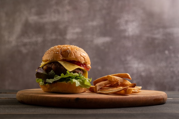 Frischer leckerer hausgemachter Hamburger mit frischem Gemüse auf einem Schneidebrett mit Pommes Frites.