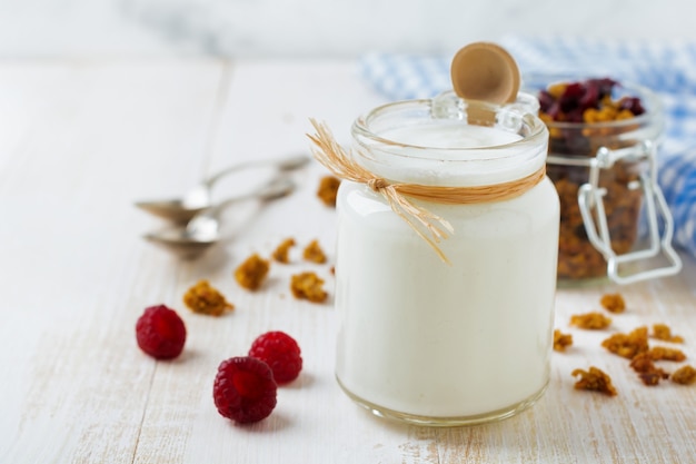 Frischer Naturjoghurt in einem Glas auf hellem Holztisch. Gesundes Essen zum Frühstück. Milchprodukte. Selektiver Fokus.