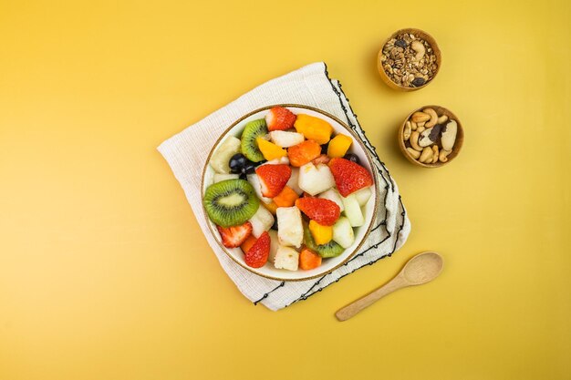 Frischer Obstsalat in einer Schüssel Bunte und tropische Früchte Ananas Mango Traube Erdbeere Papaya Melone Kiwi Zusätzlich mit Kastanien und Müsli Draufsicht Selektiver Fokus