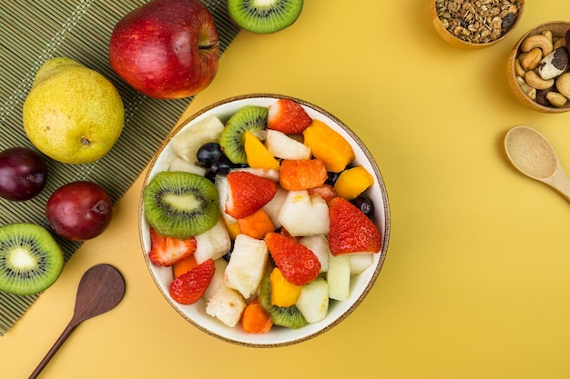 Frischer Obstsalat in einer Schüssel Bunte und tropische Früchte Ananas Mango Traube Erdbeere Papaya Melone Kiwi Zusätzlich mit Kastanien und Müsli Draufsicht Selektiver Fokus