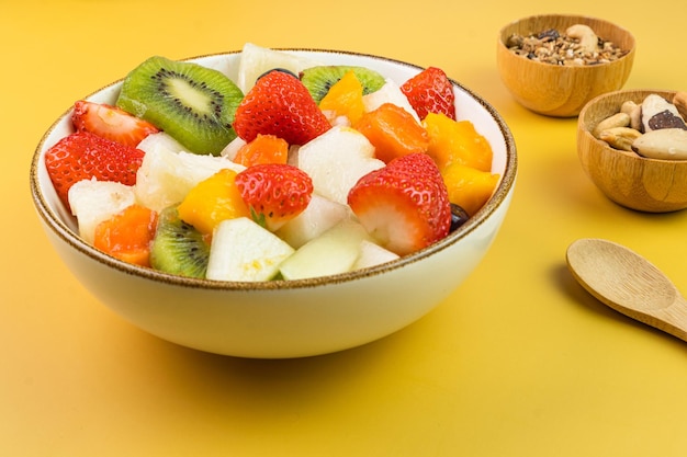 Frischer Obstsalat in einer Schüssel Bunte und tropische Früchte Ananas Mango Traube Erdbeere Papaya Melone Kiwi Zusätzlich mit Kastanien und Müsli Selektiver Fokus