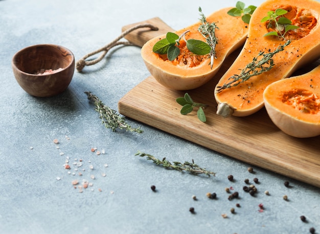 Frischer orange Muskatellerkürbis, geschnitten zur Hälfte, bereit zum Backen mit Gewürzen und Kräutern auf hölzernem Brett auf grauer Tabelle