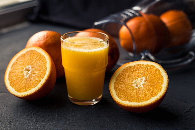 Frischer Orangensaft und frische Obstorangen auf einem schwarzen Tisch