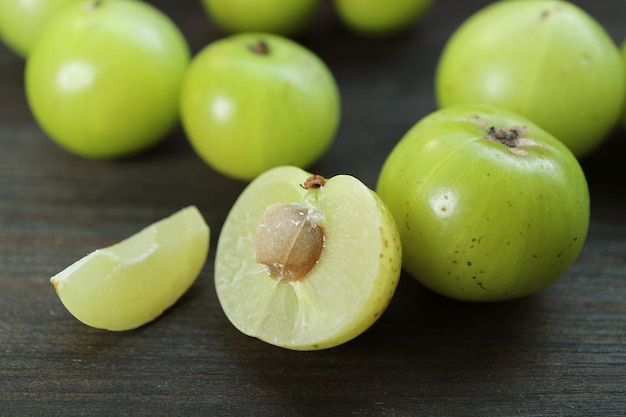 Frischer Querschnitt der Amla-Beere mit ganzen Früchten, die auf schwarzem Holzhintergrund verstreut sind