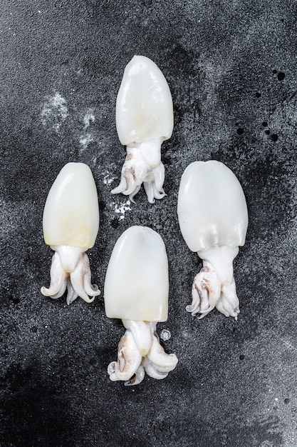 Frischer roher Mini-Tintenfisch auf dem Tisch. Schwarze Oberfläche. Draufsicht. Speicherplatz kopieren