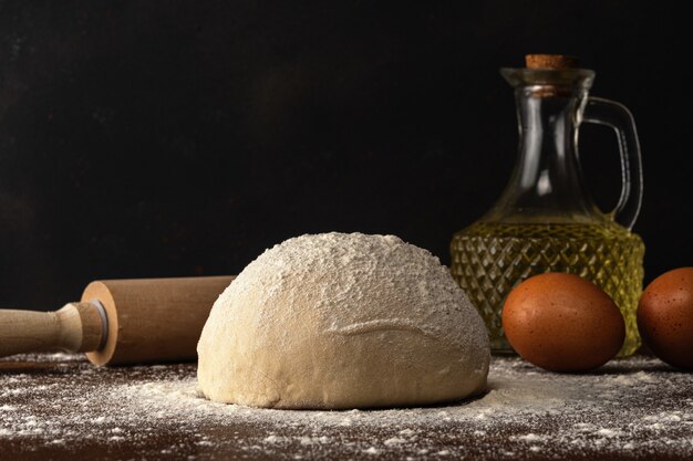 Frischer roher Teig für Brot oder Pizza mit Eiern und Öl auf einem dunklen Holztisch