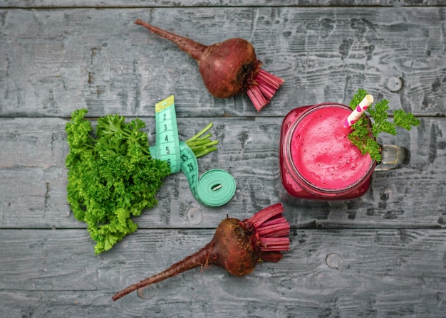 Frischer Rote-Bete-Smoothie, Maßband, zwei Rüben und Petersilie auf schwarzem Holztisch.