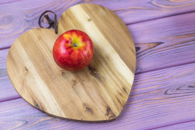 Frischer roter Apfel auf einem hölzernen Hintergrund in Form eines Herzens