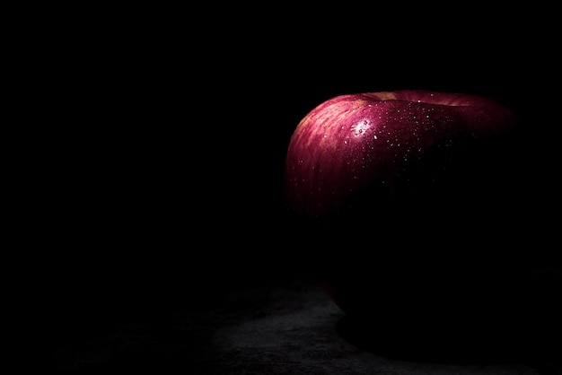 Frischer roter Apfel Auf einem schwarzen Hintergrund mit Wassertröpfchen fallen Lichter mit Platz für Text