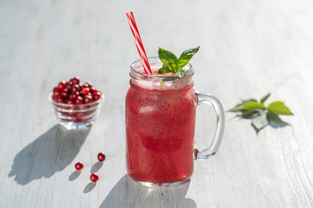 Frischer roter Bio-Smoothie im Glasbecher auf weißem Tisch, Nahaufnahme. Erfrischendes sommerliches Fruchtgetränk. Das Konzept der gesunden Ernährung. Cranberry- und Himbeer-Smoothie am sonnigen Tag