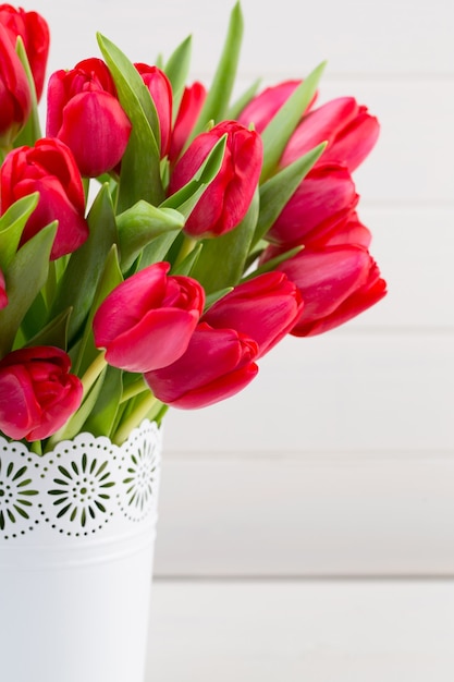 Frischer roter Tulpenblumenstrauß auf Regal vor Holzwand.