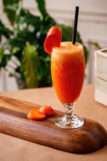 Frischer Saft der gesunden Karotte auf elegantem Glas in einem hölzernen Hintergrund. Auf der Speisekarte stehen authentische Getränke der mediterranen Küche.