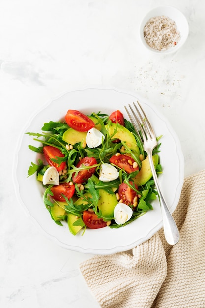 Frischer Salat aus Rucola, Tomate, Avocado, Olivenöl, Nüssen und Wachteleiern auf einer hellen Steinoberfläche